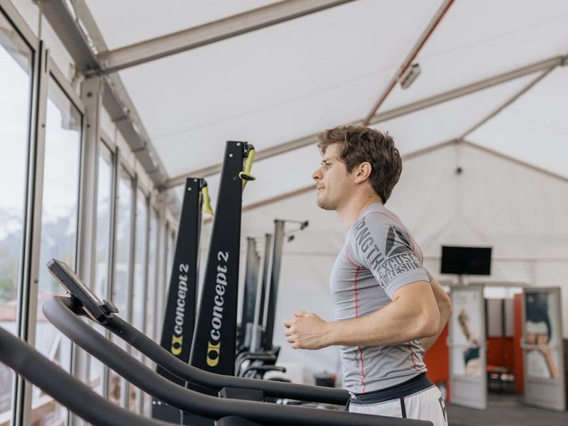 Person running on a treadmill in a modern gym with large windows.